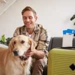 Happy young man is packed for travel, petting his golden retriever